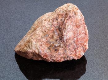 macro shooting of natural mineral rock specimen - raw pink Granite stone on dark granite background