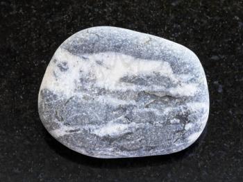 macro shooting of natural mineral rock specimen - pebble of gray Gneiss stone on dark granite background