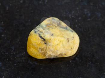 macro shooting of natural mineral rock specimen - tumbled yellow Agate gemstone on dark granite background from Mexico