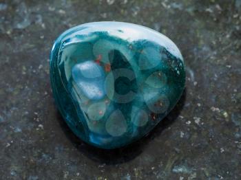 macro shooting of natural mineral rock specimen - tumbled heliotrope gemstone on dark granite background