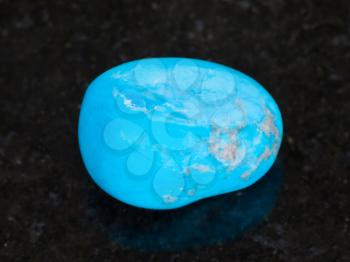 macro shooting of natural mineral rock specimen - tumbled Turquenite (blue howlite) gem stone on dark granite background