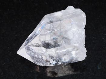 macro shooting of natural mineral rock specimen - raw rock crystal of quartz gemstone on dark granite background
