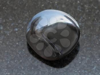 macro shooting of natural mineral rock specimen - polished obsidian (volcanic glass) gemstone on dark granite background
