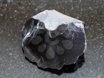 macro shooting of natural mineral rock specimen - raw obsidian (volcanic glass) crystal on dark granite background