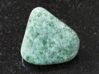macro shooting of natural mineral rock specimen - tumbled green Jadeite gemstone on dark granite background