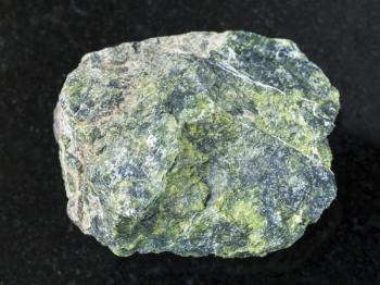 macro shooting of natural mineral rock specimen - rough serpentine stone on dark granite background