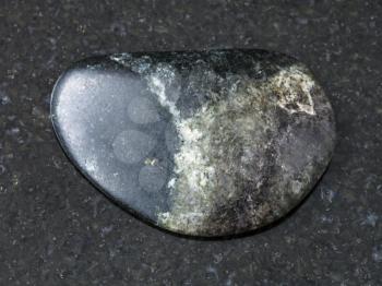 macro shooting of natural mineral rock specimen - tumbled olivinite stone on dark granite background from Kovdor region, Kola Peninsula, Russia