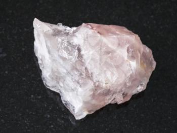 macro shooting of natural mineral rock specimen - rough crystal of rose quartz gemstone on dark granite background from Kiv-Guba mine, Karelia, Russia