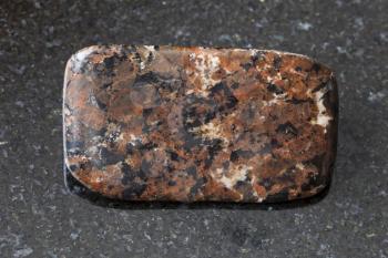 macro shooting of natural mineral rock specimen - tumbled spreusteined urtite stone on dark granite background from Khibiny Mountains, Kola Peninsula, Russia
