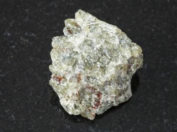 macro shooting of natural mineral rock specimen - raw olivine stone on dark granite background from Kovdor region, Kola Peninsula, Russia