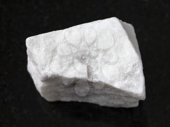 macro shooting of natural mineral rock specimen - piece of raw white marble stone on dark granite background