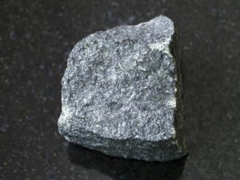 macro shooting of natural mineral rock specimen - rough Gabbro stone on dark granite background