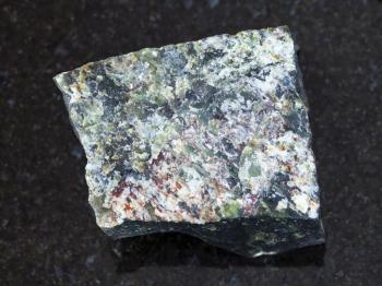 macro shooting of natural mineral rock specimen - raw dunite stone on dark granite background