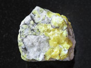 macro shooting of natural mineral rock specimen - raw sulfur ore on dark granite background from Volodinskoye mine, Samara region, Russia
