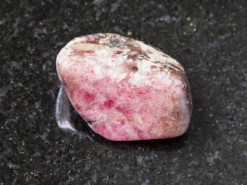 macro shooting of natural mineral rock specimen - tumbled pink rhodonite gem stone on dark granite background from Ural mountains in Russia