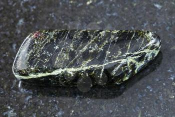 macro shooting of natural mineral rock specimen - polished Diopside gemstone on dark granite background Kovdor region, Karelia, Russia