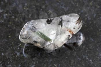 macro shooting of natural mineral rock specimen - tumbled quartz gemstone with Tourmaline crystals (tourmalinated quartz) on dark granite background