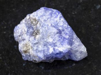 macro shooting of natural mineral rock specimen - raw crystal of Tanzanite gemstone on dark granite background from Tanzania