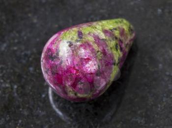 macro shooting of natural mineral rock specimen - polished pink and green zoisite gemstone on dark granite background
