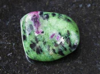 macro shooting of natural mineral rock specimen - polished zoisite (anyolite) gemstone on dark granite background