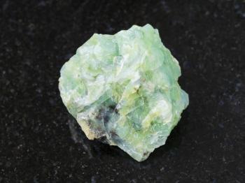 macro shooting of natural mineral rock specimen - rough crystal of chrysopal gemstone on dark granite background from Pstan mine, Kazakhstan