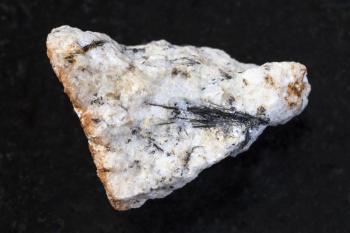 macro shooting of natural mineral rock specimen - black Ludwigite crystals in raw stone on dark granite background from Praskovie-Evgenyevskaya mine, South Ural, Russia