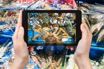 travel concept - tourist photographs crab on Huangsha Aquatic Product Trading Market in Guangzhou city in China in spring season on tablet