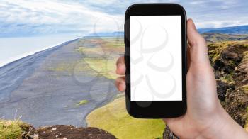 travel concept - tourist photographs Solheimafjara black sand beach from Dyrholaey cliff on Atlantic Coast in Iceland in autumn on smartphone with cut out screen for advertising logo