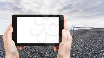 travel concept - tourist photographs Reynisfjara Beach and view of Dyrholaey promontory in Iceland on Atlantic South Coast in autumn on tablet with cut out screen for advertising logo