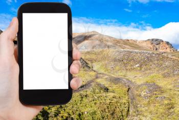 travel concept - tourist photographs trails in Landmannalaugar area of Fjallabak Nature Reserve in Highlands region of Iceland in autumn on smartphone with cut out screen for advertising logo