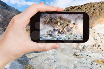 travel concept - tourist photographs acidic mudpot in geothermal Krysuvik area on Southern Peninsula (Reykjanesskagi, Reykjanes Peninsula) in Iceland in september on smartphone