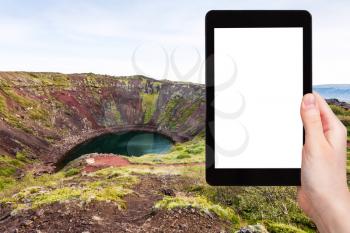 travel concept - tourist photographs volcanic crater with Kerid lake in Iceland in autumn on tablet with cut out screen for advertising logo