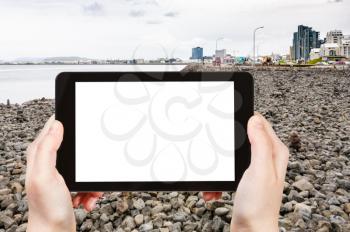 travel concept - tourist photographs stone beach at Sculpture and Shore Walk on Atlantic coast in Reykjavik city in Iceland in september on tablet with cut out screen for advertising logo