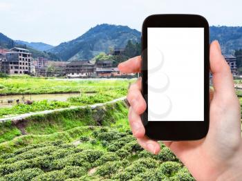 travel concept - tourist photographs tea and rice fields near irrigation canal in Chengyang village of Sanjiang Dong Autonomous County in China in spring on smartphone with cut out screen