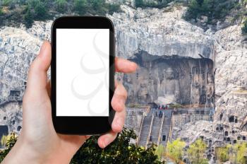 travel concept - tourist photographs West Hill with The Big Vairocana statue of Chinese Buddhist monument Longmen Caves (Dragon's Gate Grottoes) on smartphone with cut out screen for advertising logo