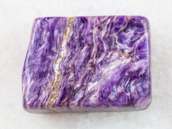 macro shooting of natural mineral rock specimen - polished slab of charoite gemstone on white marble background from Murun Massif, Yakutia, Russia