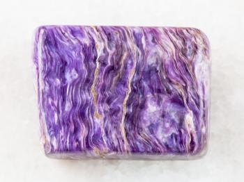 macro shooting of natural mineral rock specimen - tumbled slab of charoite gemstone on white marble background from Murun Massif, Yakutia, Russia