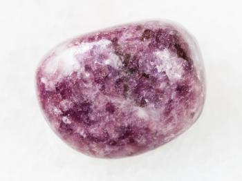 macro shooting of natural mineral rock specimen - tumbled Lepidolite gemstone on white marble background from Brazil