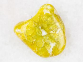 macro shooting of natural mineral rock specimen - polished yellow Lizardite gemstone on white marble background