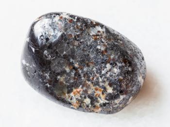 macro shooting of natural mineral rock specimen - tumbled magnetite stone on white marble background from Kovdor district of Kola Peninsula, Russia