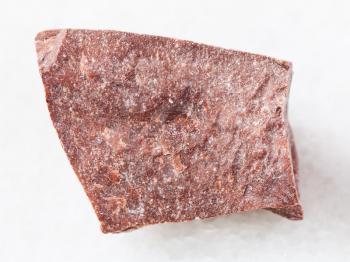 macro shooting of natural mineral rock specimen - piece of raw red marble stone on white marble background