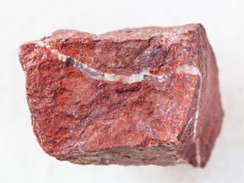 macro shooting of natural mineral rock specimen - raw red jasper stone on white marble background