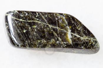 macro shooting of natural mineral rock specimen - tumbled Diopside gemstone on white marble background Kovdor region, Karelia, Russia