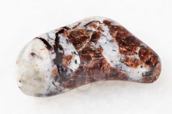 macro shooting of natural mineral rock specimen - tumbled Eudialyte in syenite stone on white marble background from Khibiny Mountains, Kola Peninsula, Russia