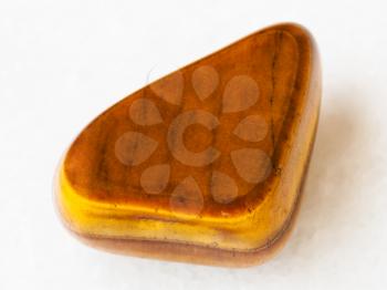 macro shooting of natural mineral rock specimen - tumbled tiger-eye gem stone on white marble background from South Africa