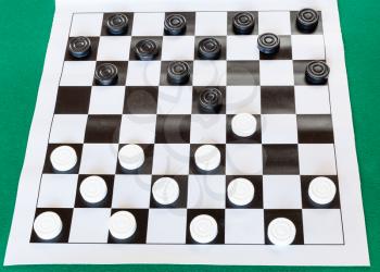 white checkered sheet board with draughts on green baize table