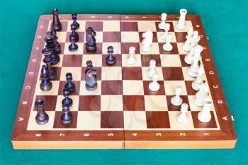 side view of chess gameplay on wooden chessboard on green baize table