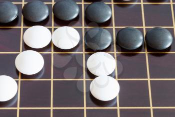 gameplay of Go game on brown wooden board close up