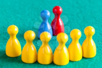 concept scene - pair from blue and red pawns in front of several yellow pawns on green baize table. Focus on the pair.