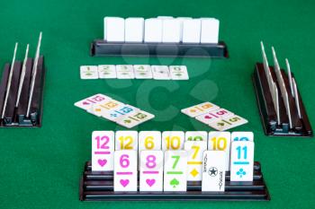 tiles in rack and gameplay in Rummy tile-based card game on green baize table. Rummy is tile and card game based on matching cards of the same rank or sequence and same suit